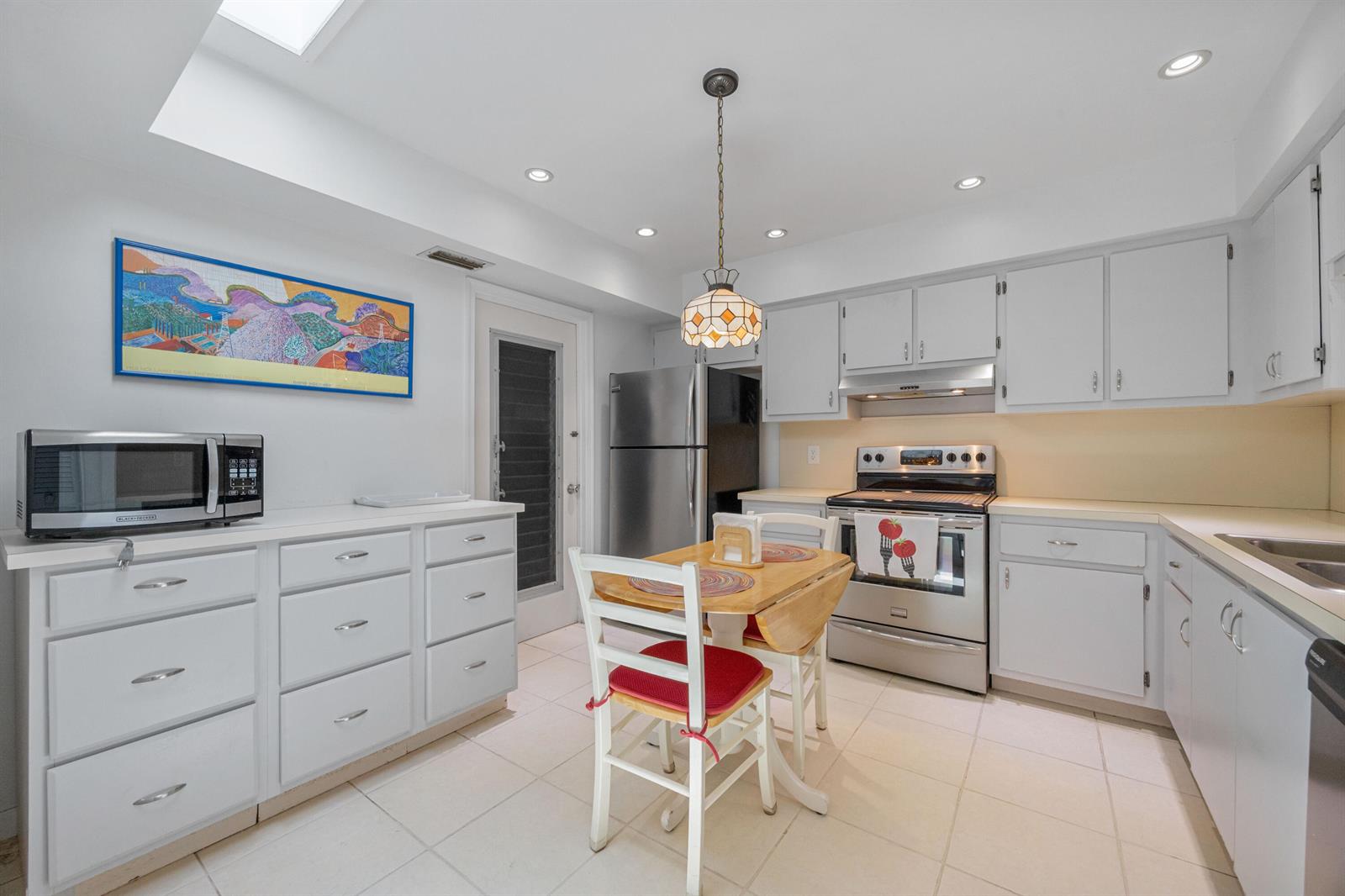 A kitchen with white cabinets, stainless steel appliances, a small dining table, and tile flooring — 22 Ridge Pointe Drive # C, Boynton Beach FL 33435, BOYNTON BEACH, FL