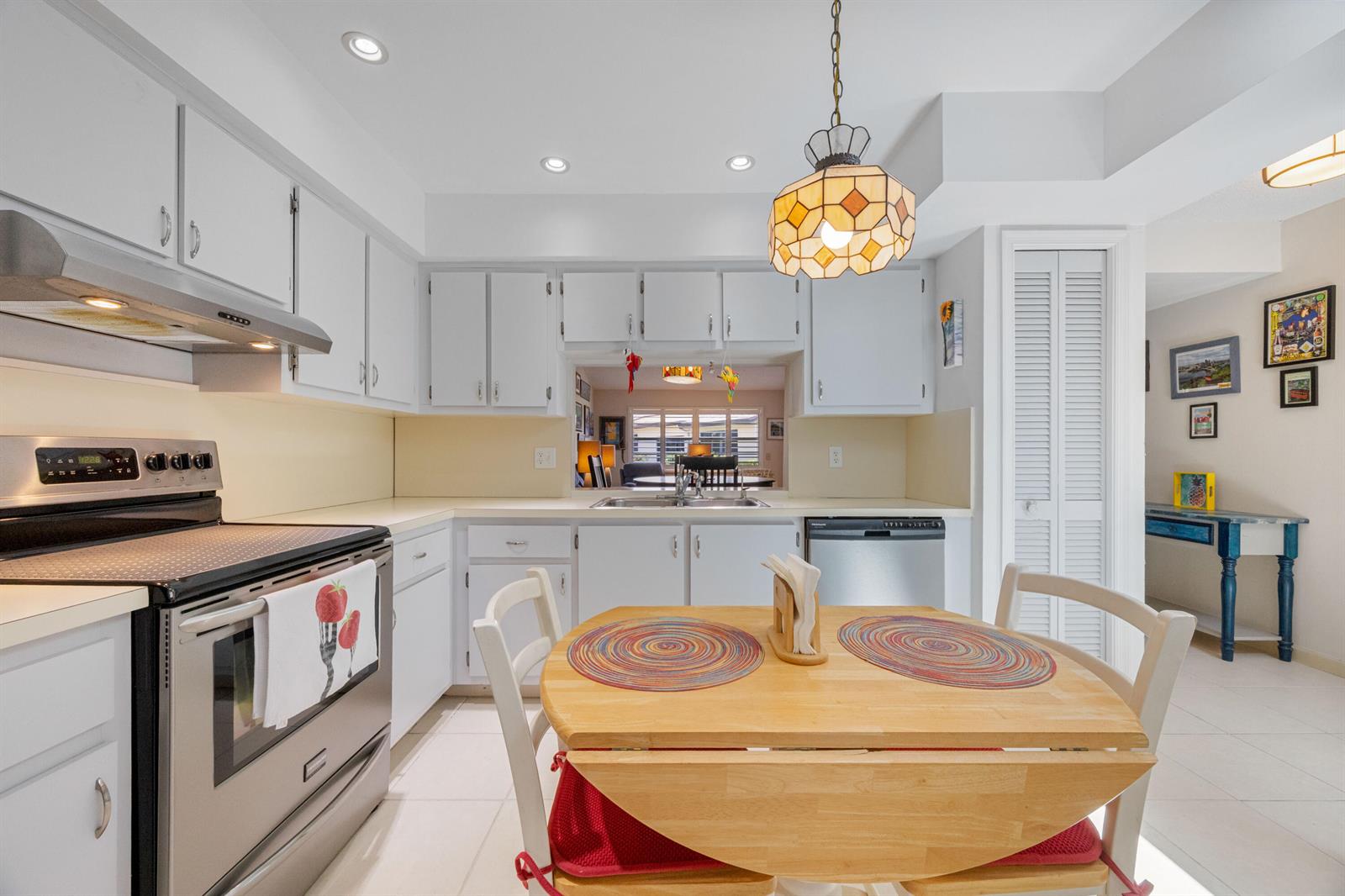 A kitchen features white cabinetry, stainless steel appliances, a pass-through window, and a dining table — 22 Ridge Pointe Drive # C, Boynton Beach FL 33435, BOYNTON BEACH, FL