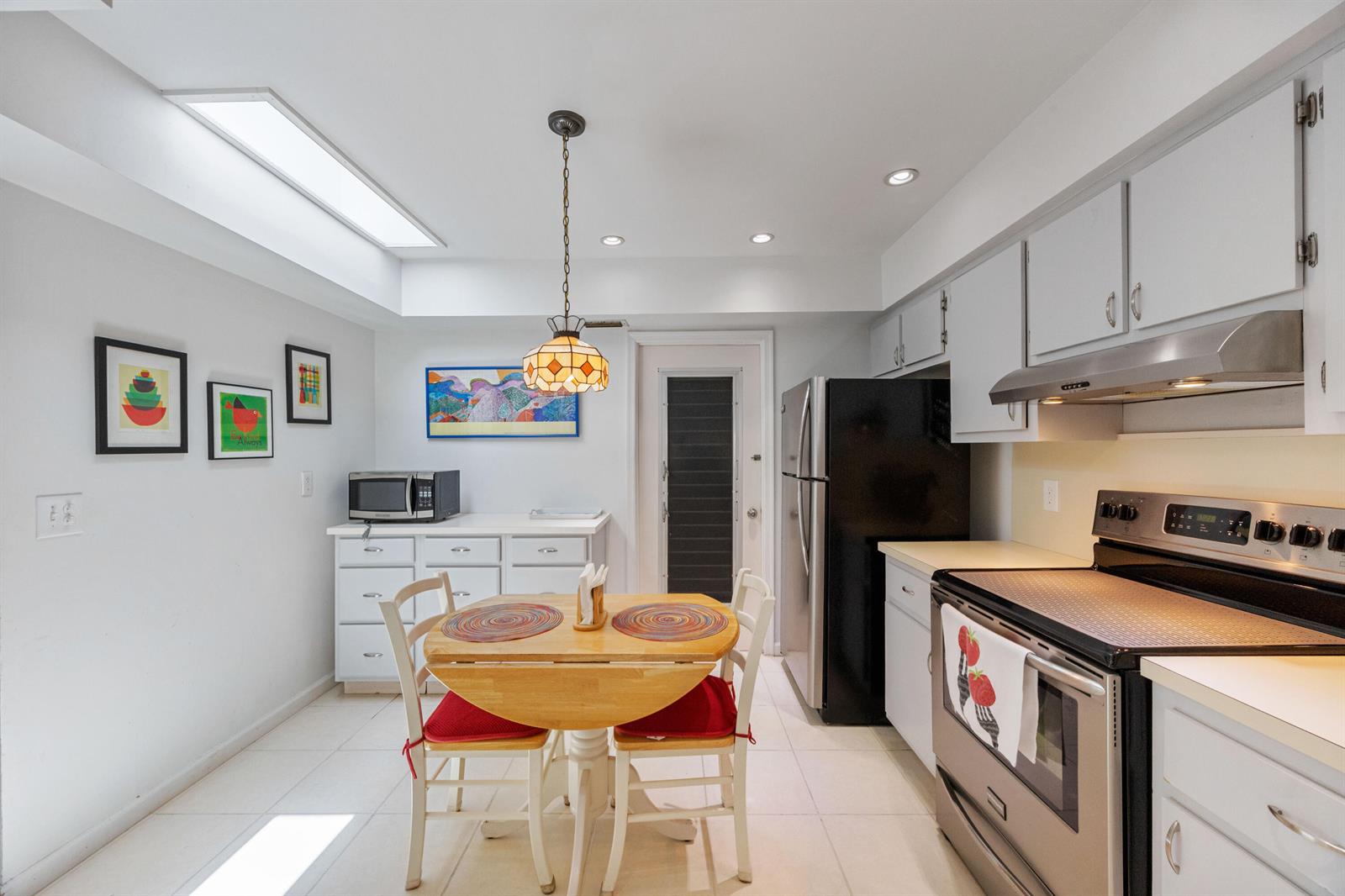 A kitchen with white cabinets, stainless steel appliances, a small dining table, and a skylight — 22 Ridge Pointe Drive # C, Boynton Beach FL 33435, BOYNTON BEACH, FL