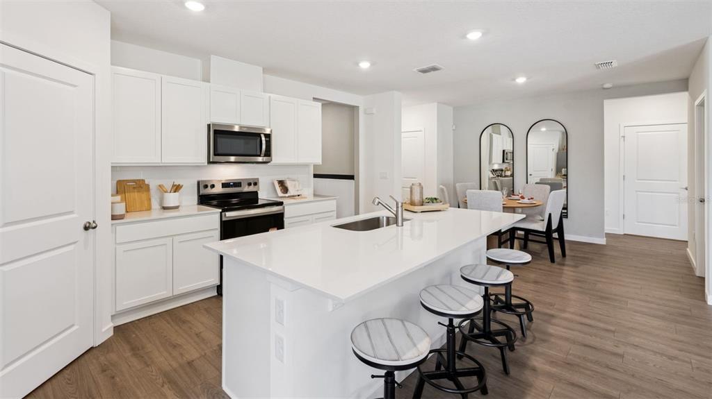 A modern kitchen features white cabinetry, a large quartz island, and barstool seating — 2928 ELIO HAMMOCK DRIVE, ST CLOUD, FL