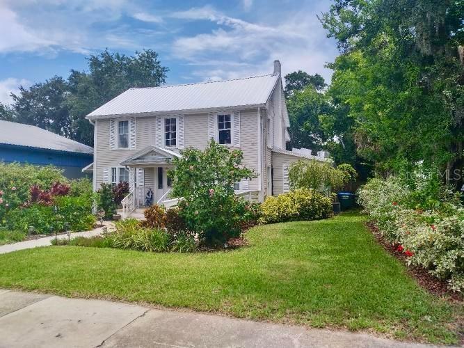 A two-story house with light siding and a white metal roof sits on a lawn — 317 N ORANGE STREET, NEW SMYRNA BEACH, FL