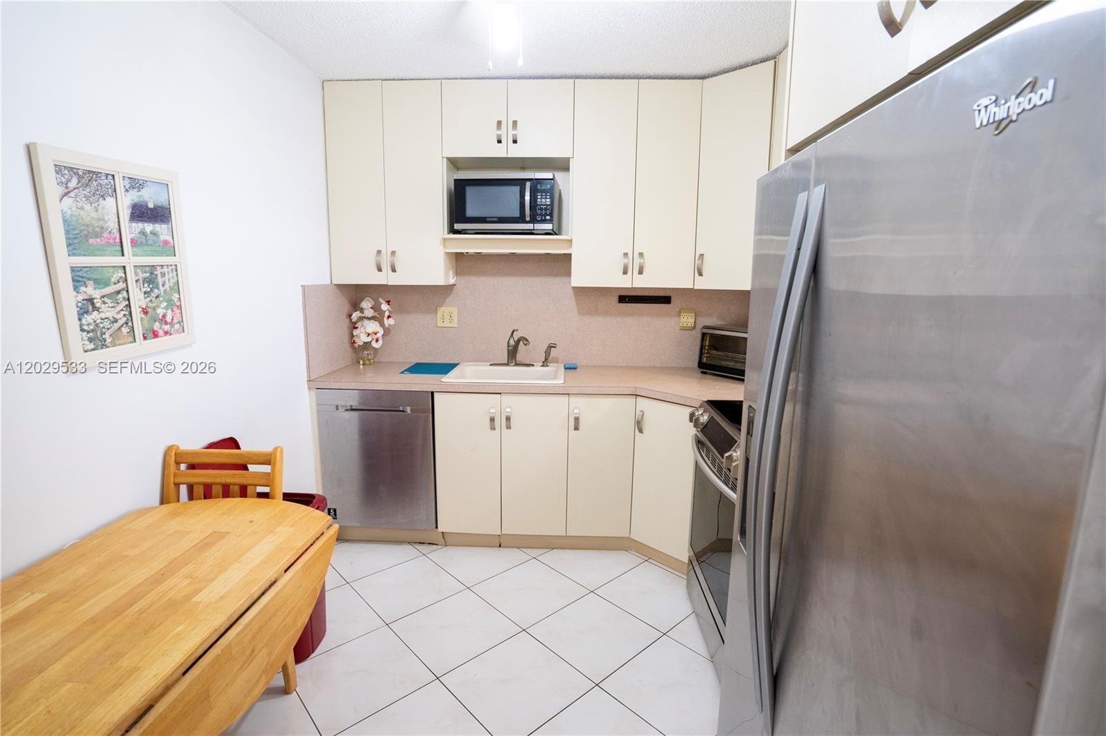 A kitchen features off-white cabinets, stainless steel appliances, and a wooden dining table — 600 Three Islands Blvd # 1416, Hallandale Beach FL 33009, HALLANDALE BEACH, FL