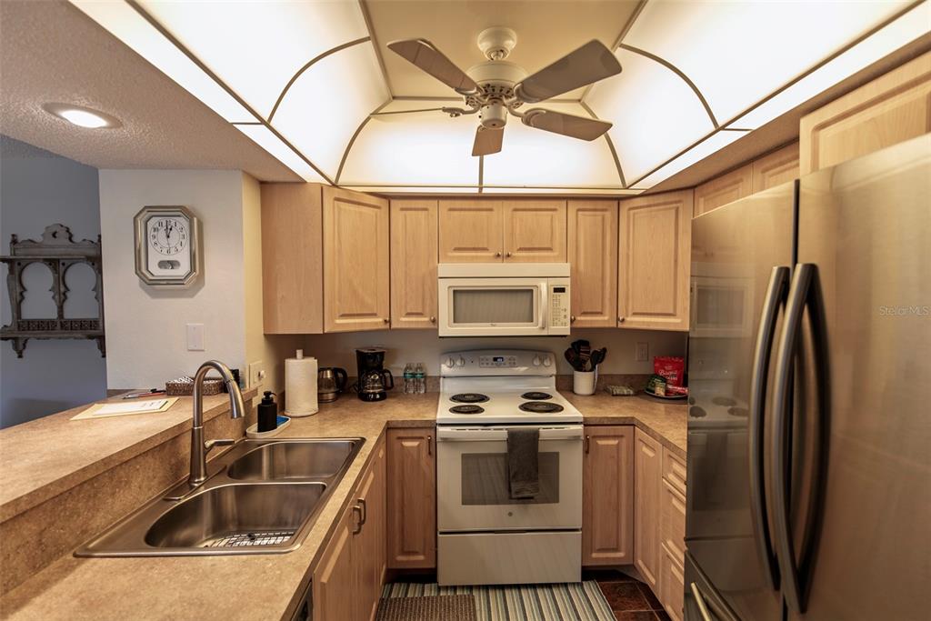 A kitchen features light wood cabinets, white appliances, a double sink, and a ceiling fan — 19505 QUESADA AVENUE UNIT AA105, PORT CHARLOTTE, FL