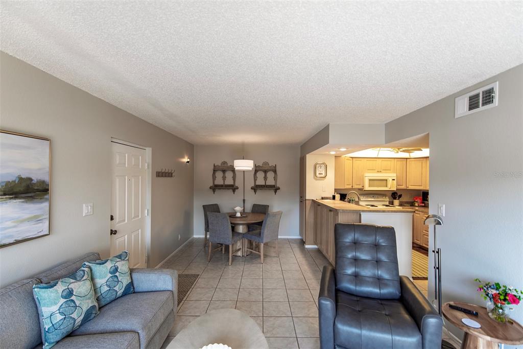 A living room and dining area with tile floors, a grey sofa, and an open kitchen — 19505 QUESADA AVENUE UNIT AA105, PORT CHARLOTTE, FL
