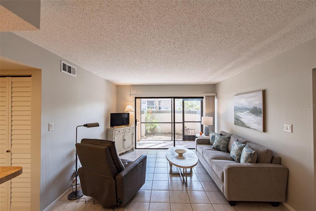 A living room features tile flooring, a grey sofa, a recliner, and a sliding glass door — 19505 QUESADA AVENUE UNIT AA105, PORT CHARLOTTE, FL