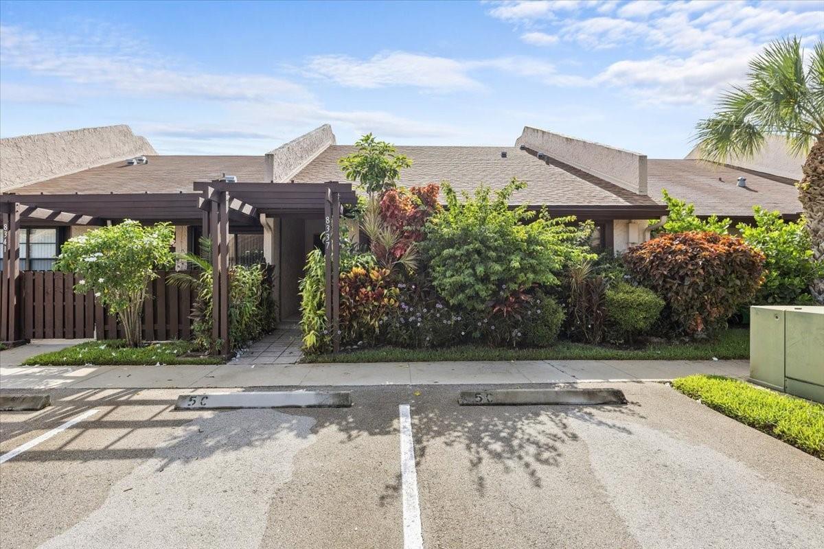 A single-story townhouse exterior features a wooden pergola, lush landscaping, and assigned parking spaces — 8337 NW 37th Place # 8337, Sunrise FL 33351, SUNRISE, FL