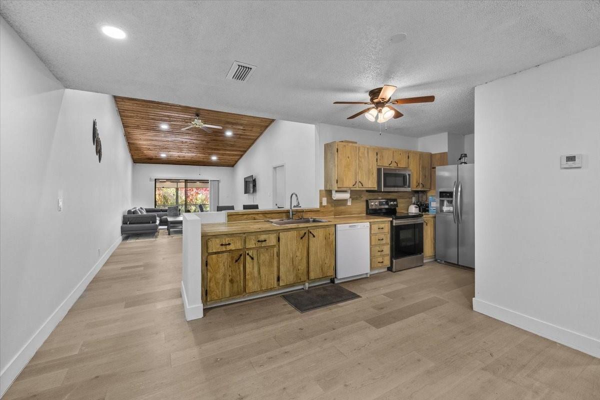 A kitchen with wood cabinets and light flooring opens into a living area with vaulted ceilings — 8337 NW 37th Place # 8337, Sunrise FL 33351, SUNRISE, FL