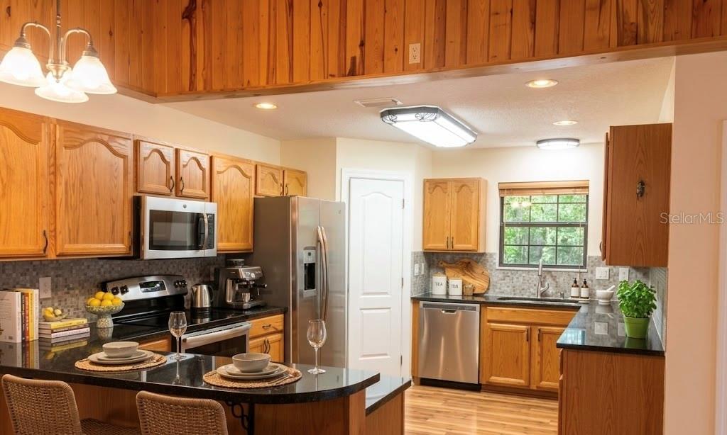 A kitchen features wood cabinets, black countertops, stainless steel appliances, and a wood-paneled ceiling — 6611 SW 80TH AVENUE, OCALA, FL