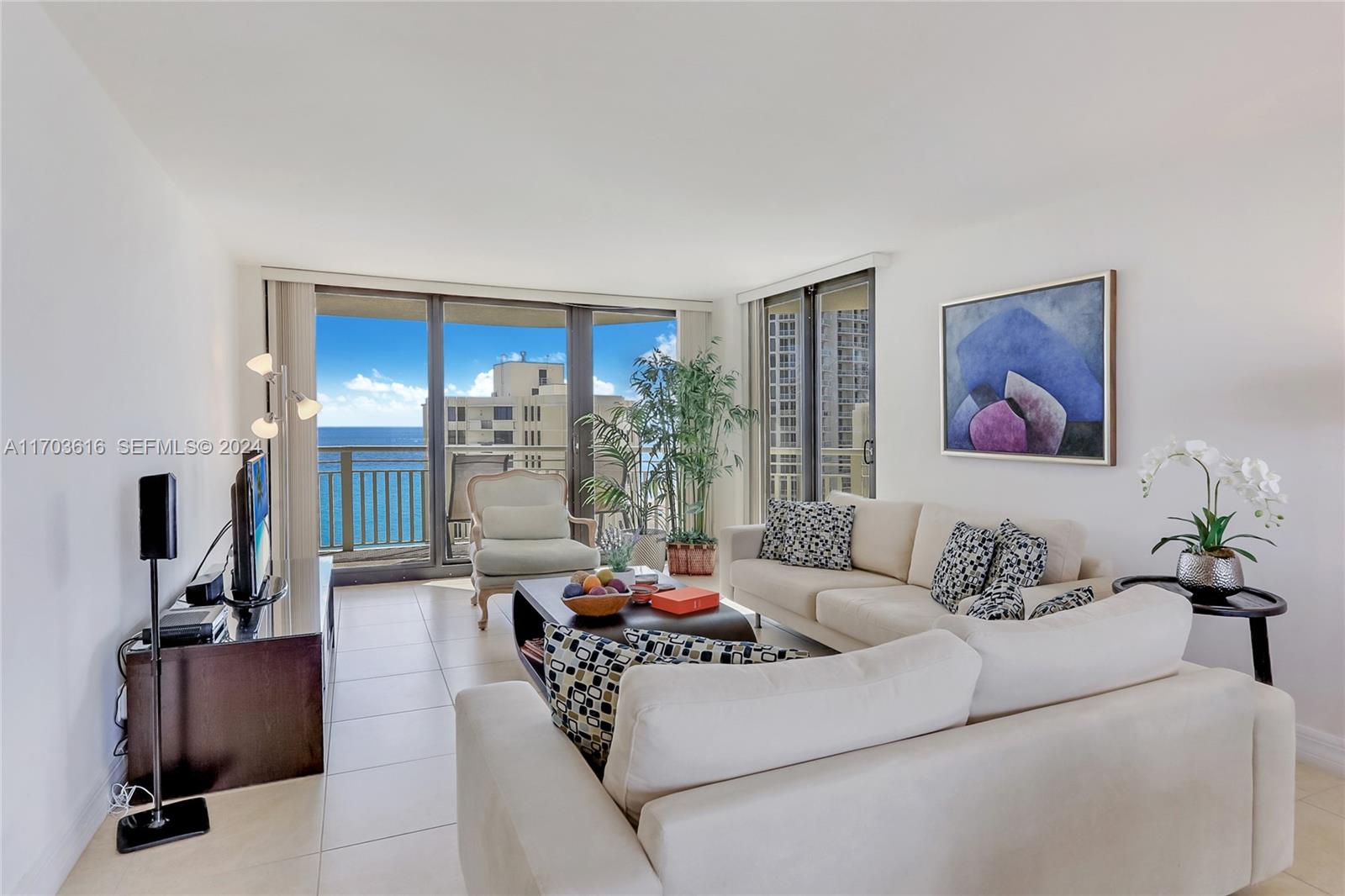 A bright living room features white sofas, a coffee table, and a balcony with ocean views — 3000 N Ocean Dr # 24H, Riviera Beach FL 33404, RIVIERA BEACH, FL