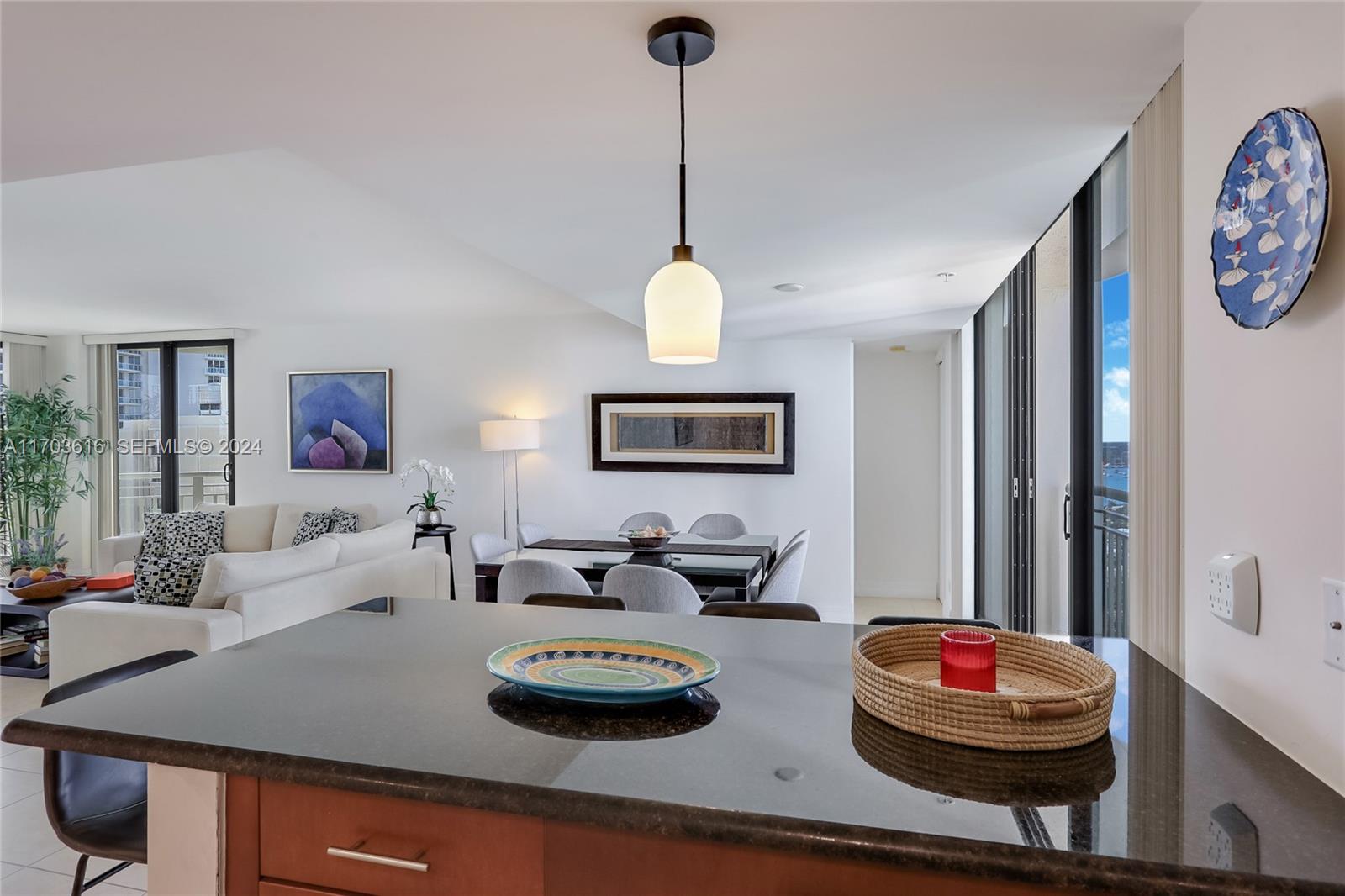 A kitchen island with a dark countertop overlooks a dining area and living room — 3000 N Ocean Dr # 24H, Riviera Beach FL 33404, RIVIERA BEACH, FL