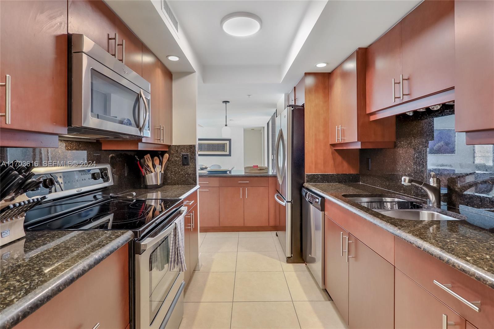A galley kitchen features cherry wood cabinets, dark granite countertops, and stainless steel appliances — 3000 N Ocean Dr # 24H, Riviera Beach FL 33404, RIVIERA BEACH, FL