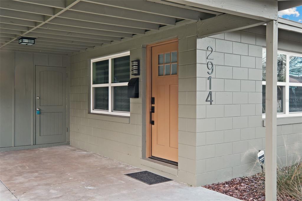 A tan front door sits next to a gray concrete block wall with house numbers — 2910 DADE AVENUE, ORLANDO, FL
