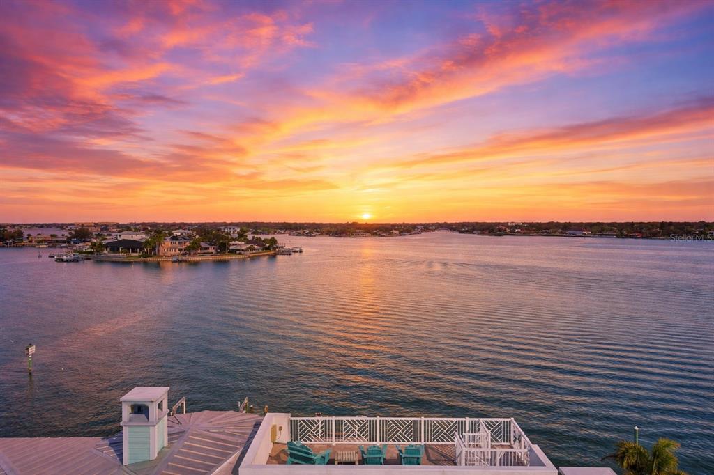 A covered patio features blue wicker sectional seating overlooking a sunset view of the water — 391 12TH AVENUE, INDIAN ROCKS BEACH, FL