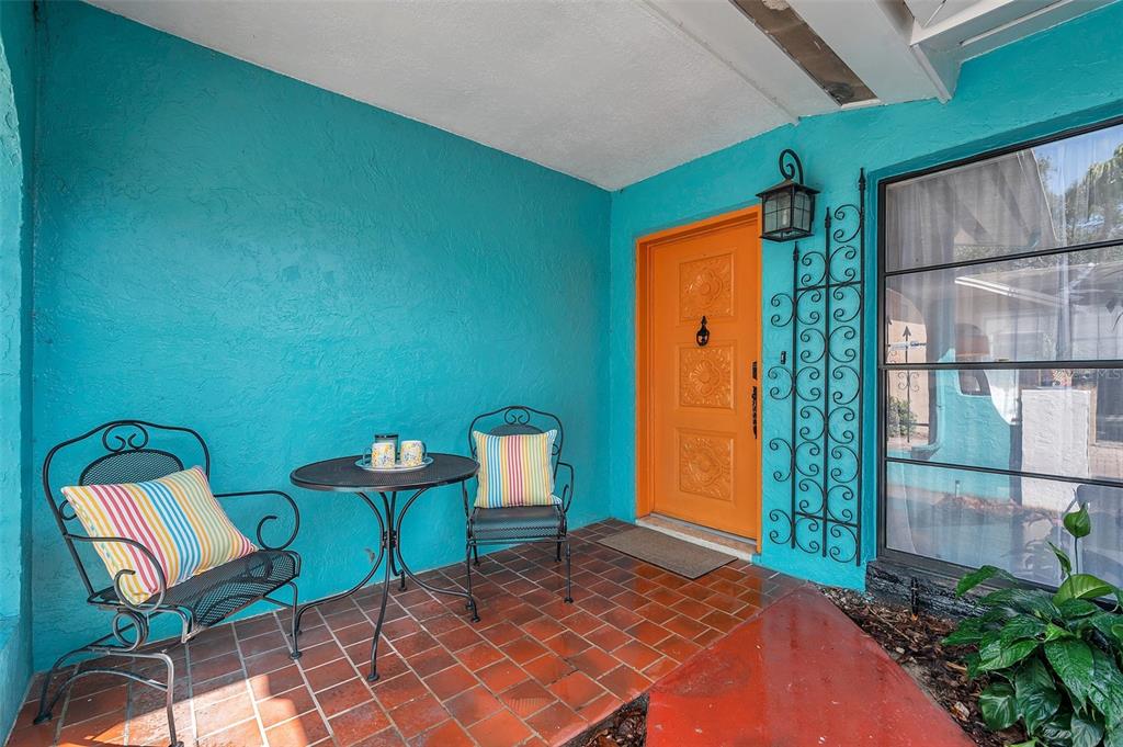 A covered porch features a bright orange front door, turquoise walls, and a bistro set — 717 CAROLINA AVENUE, TARPON SPRINGS, FL