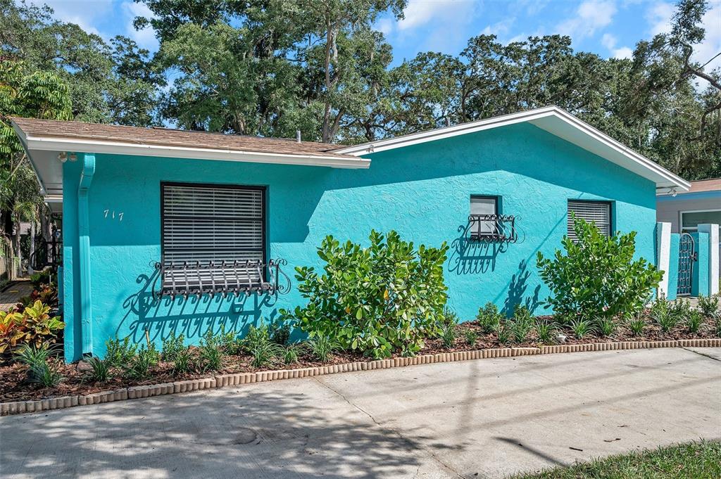 A bright turquoise house exterior features two windows with decorative metal grilles and landscaping — 717 CAROLINA AVENUE, TARPON SPRINGS, FL