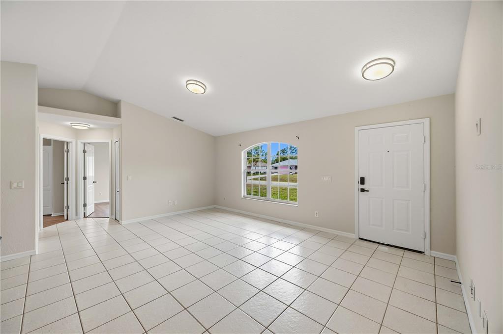 An empty living room features white tile flooring, beige walls, and a front entry door — 2260 MISTLETO LANE, NORTH PORT, FL