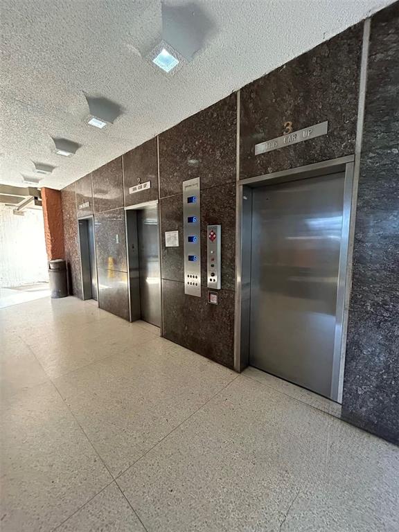 A hallway features three stainless steel elevator doors set into dark brown marble walls — 650 CUEVAS BUSTAMANTE COND. SEGOVIA UNIT 15, SAN JUAN, PR