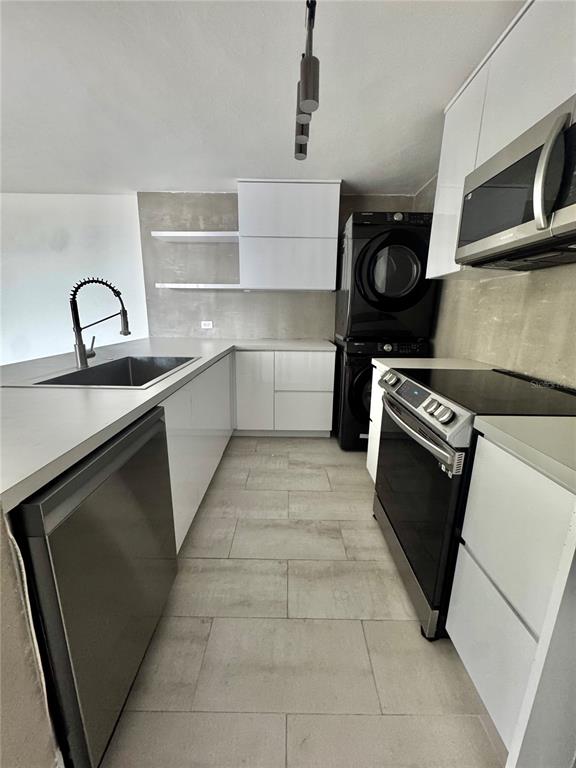 A modern kitchen features white cabinets, stainless steel appliances, a stacked washer-dryer, and tile flooring — 650 CUEVAS BUSTAMANTE COND. SEGOVIA UNIT 15, SAN JUAN, PR
