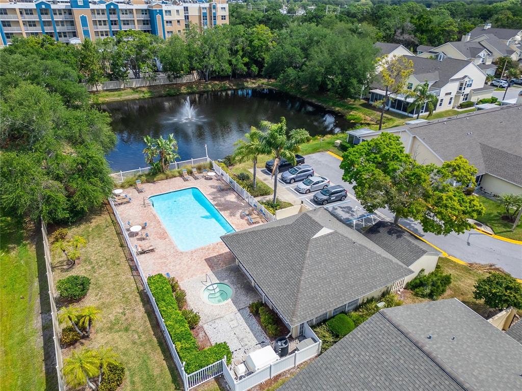 An aerial view shows a swimming pool, hot tub, and clubhouse next to a pond — 1050 STARKEY ROAD UNIT 509, LARGO, FL