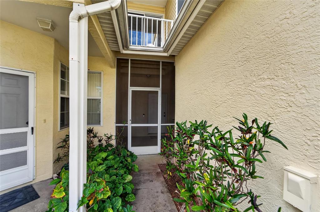A walkway leads to a screened entryway with a balcony above and yellow stucco walls — 1050 STARKEY ROAD UNIT 509, LARGO, FL