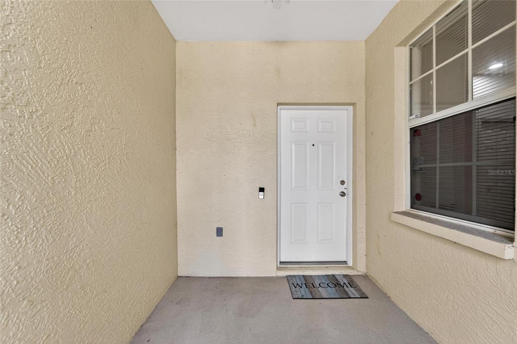 A covered entryway features a white front door, a welcome mat, and beige stucco walls — 1050 STARKEY ROAD UNIT 509, LARGO, FL