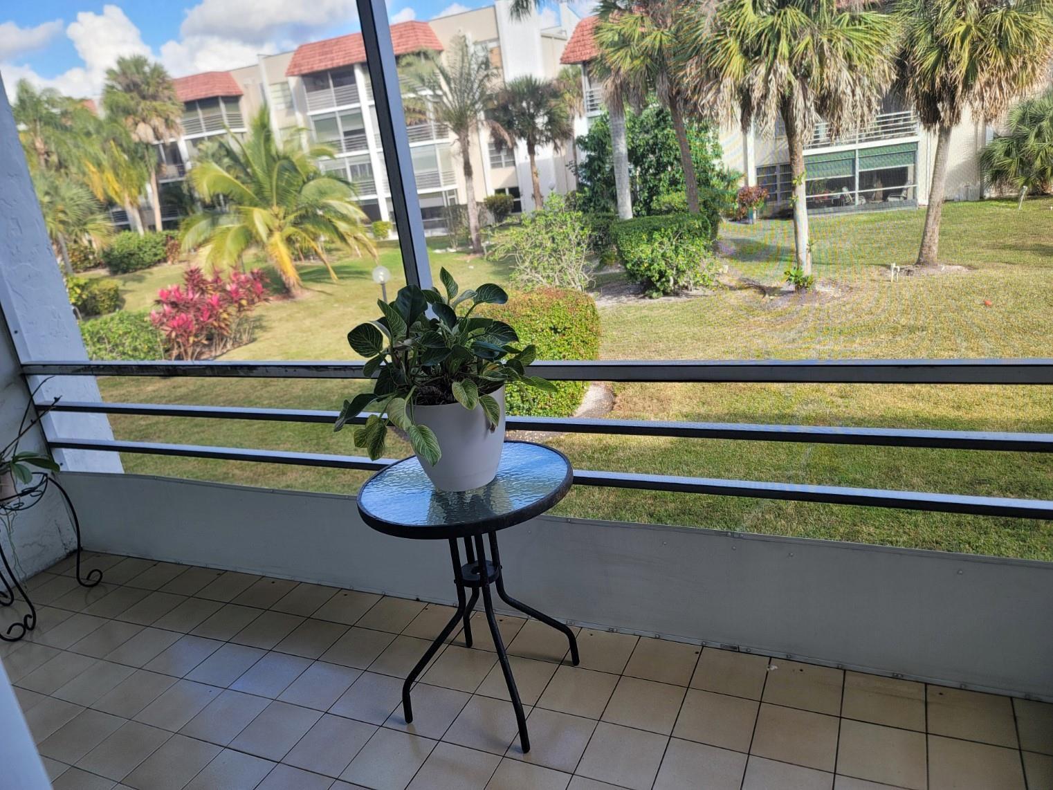 A potted plant sits on a small glass table on a screened-in balcony overlooking landscaping — 3774 Inverrary Boulevard # P202, Lauderhill FL 33319, LAUDERHILL, FL