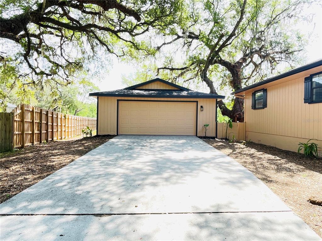 A detached garage with a tan exterior and a concrete driveway sits under large trees — 4893 S OLD FLORAL CITY ROAD, INVERNESS, FL