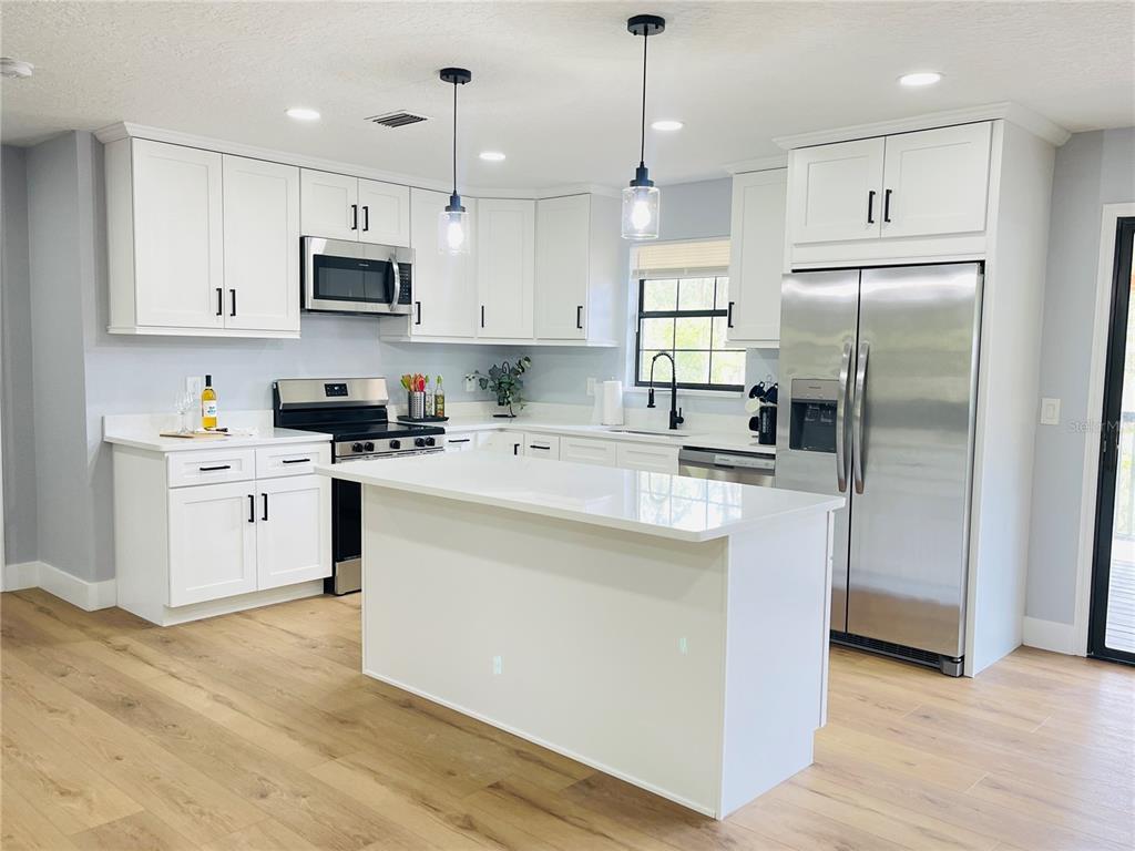 A modern kitchen features white cabinetry, stainless steel appliances, a central island, and wood flooring — 4893 S OLD FLORAL CITY ROAD, INVERNESS, FL