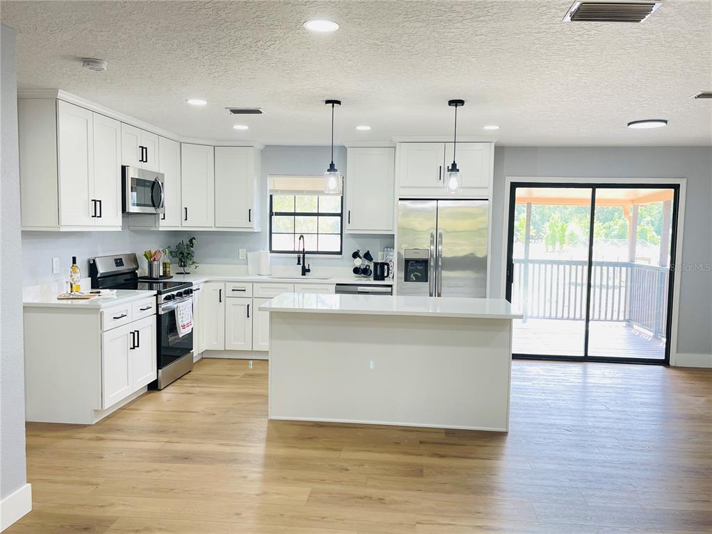 A modern kitchen features white cabinetry, stainless steel appliances, a center island, and wood flooring — 4893 S OLD FLORAL CITY ROAD, INVERNESS, FL