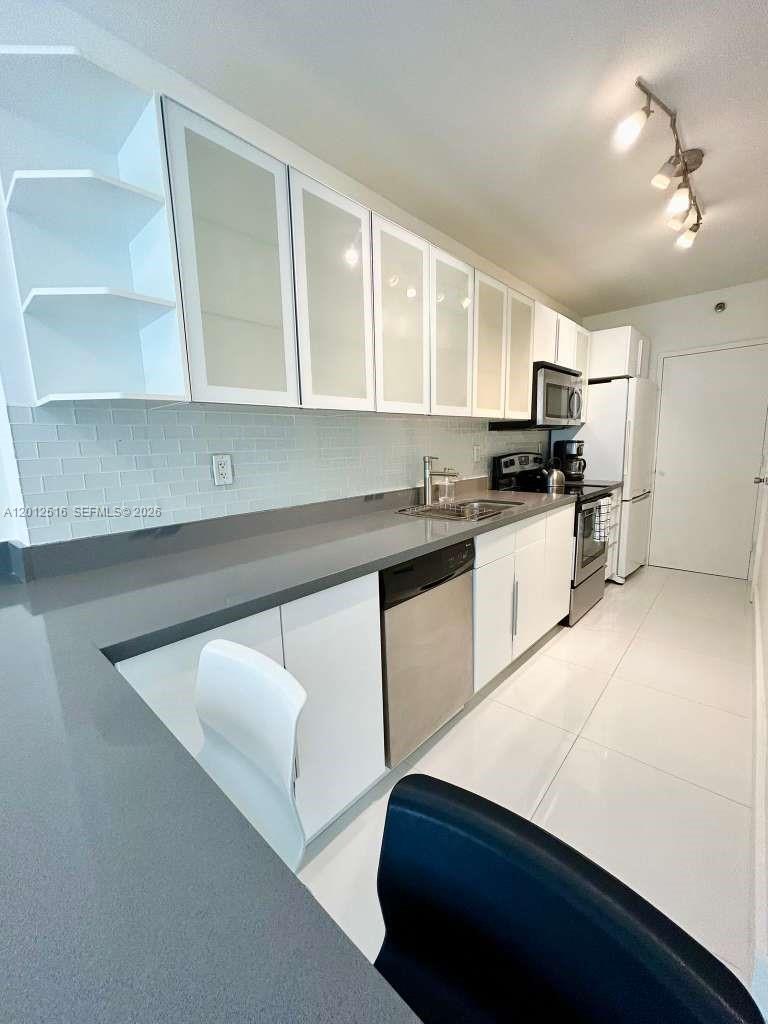 A modern kitchen features white cabinetry, gray countertops, stainless steel appliances, and white tile flooring — 100 Lincoln Rd # 526, Miami Beach FL 33139, MIAMI BEACH, FL
