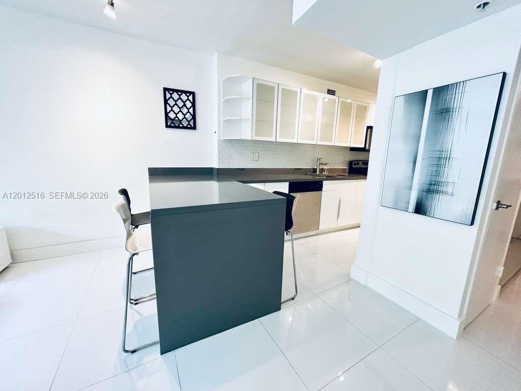 A modern kitchen features white cabinetry, a dark gray island, and glossy white tile flooring — 100 Lincoln Rd # 526, Miami Beach FL 33139, MIAMI BEACH, FL
