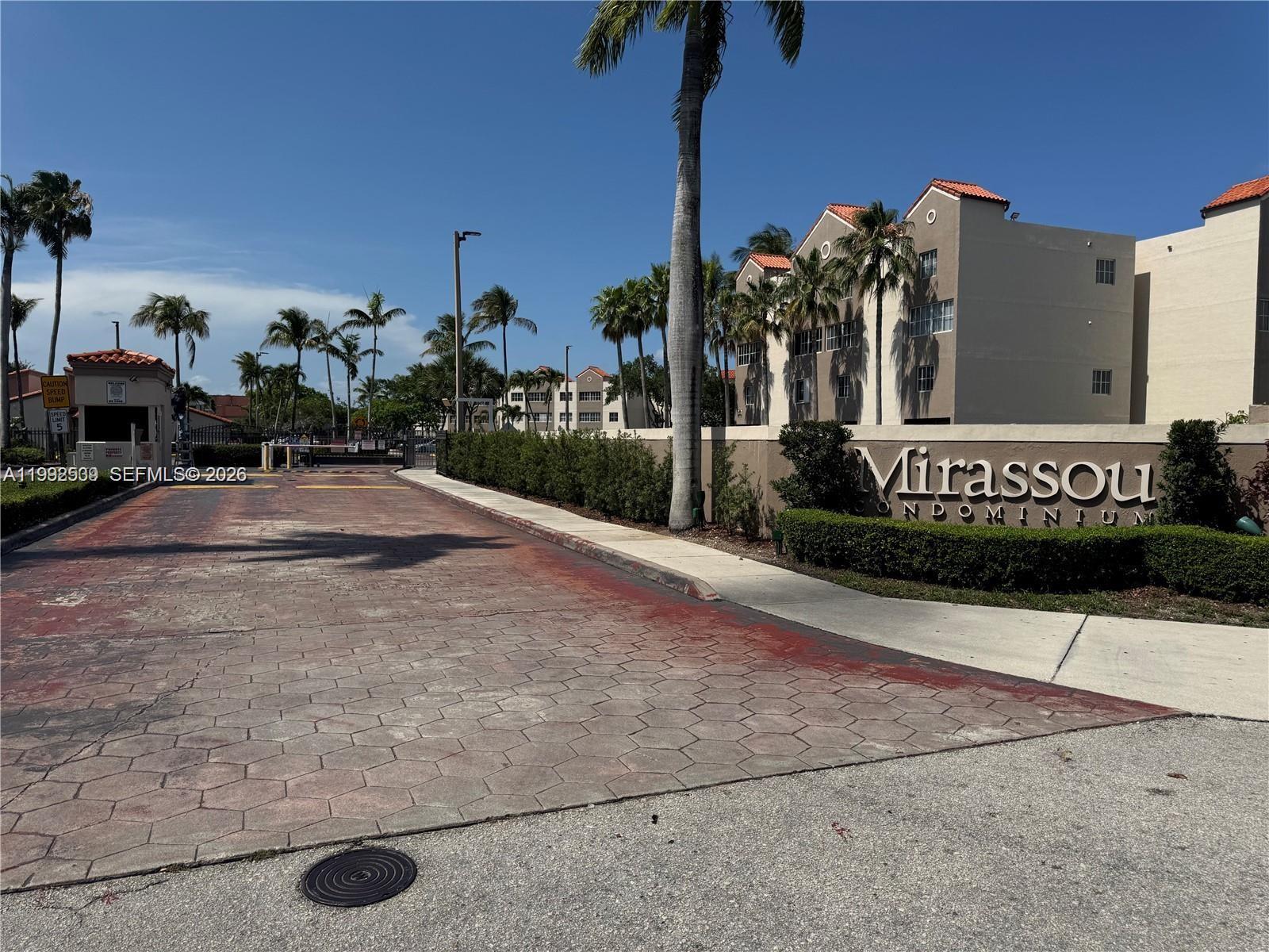 The entrance to the Mirassou Condominium features a paved driveway, palm trees, and signage — 6155 NW 186th St # 207, Hialeah FL 33015, HIALEAH, FL