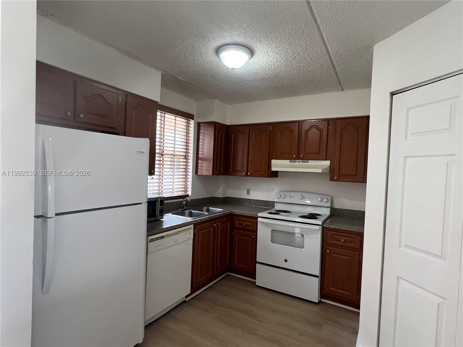 A kitchen features wood cabinets, white appliances, a double sink, and light-colored wood flooring — 6155 NW 186th St # 207, Hialeah FL 33015, HIALEAH, FL