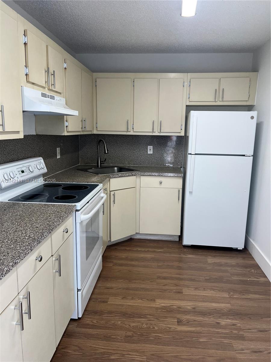 A kitchen features light-colored cabinets, a white stove, a white refrigerator, and wood-look flooring — 6141 W 22nd Ct # 202, Hialeah FL 33016, HIALEAH, FL