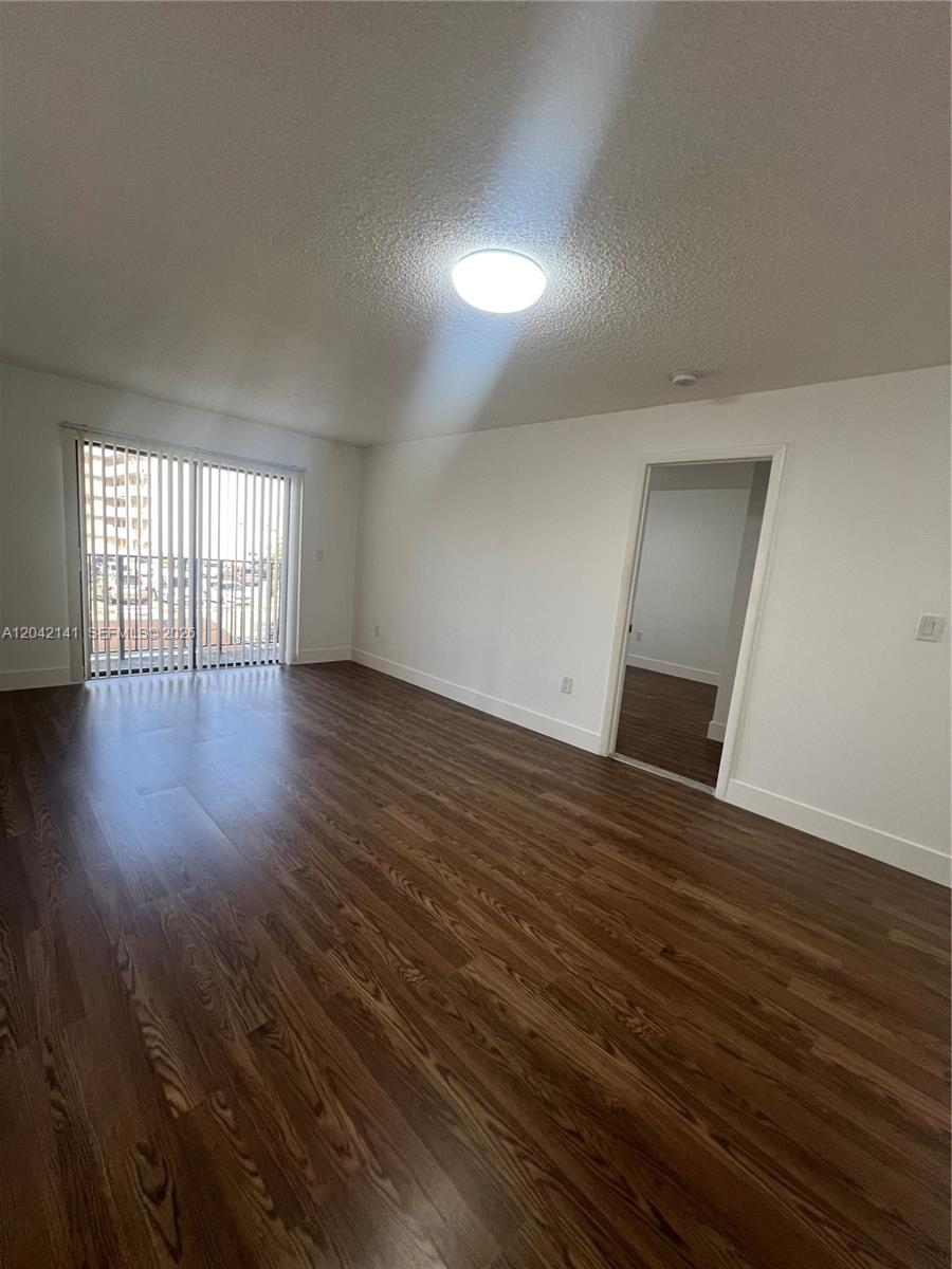 An empty room features wood-look flooring, white walls, a ceiling light, and a sliding glass door — 6141 W 22nd Ct # 202, Hialeah FL 33016, HIALEAH, FL