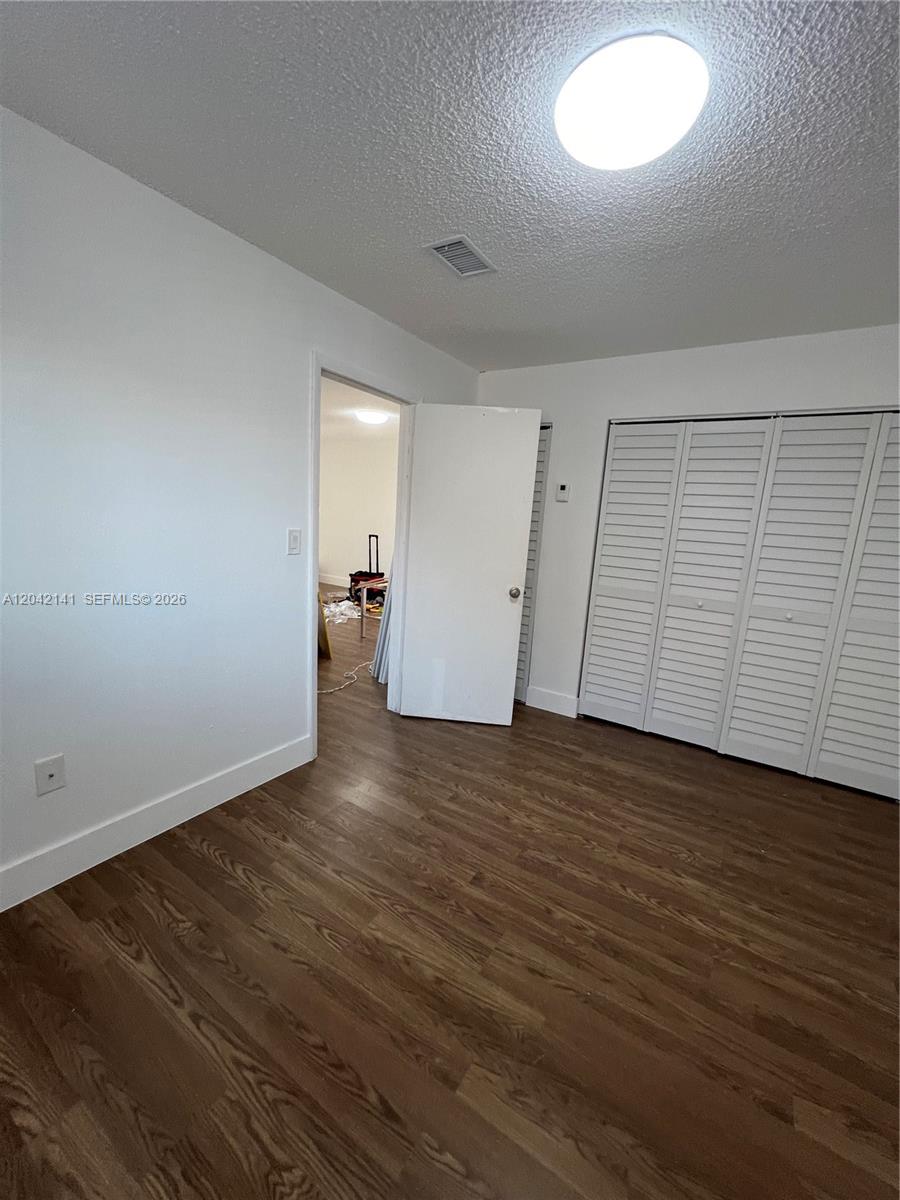 This bedroom features white walls, wood-look flooring, a ceiling light, and white louvered closet doors — 6141 W 22nd Ct # 202, Hialeah FL 33016, HIALEAH, FL