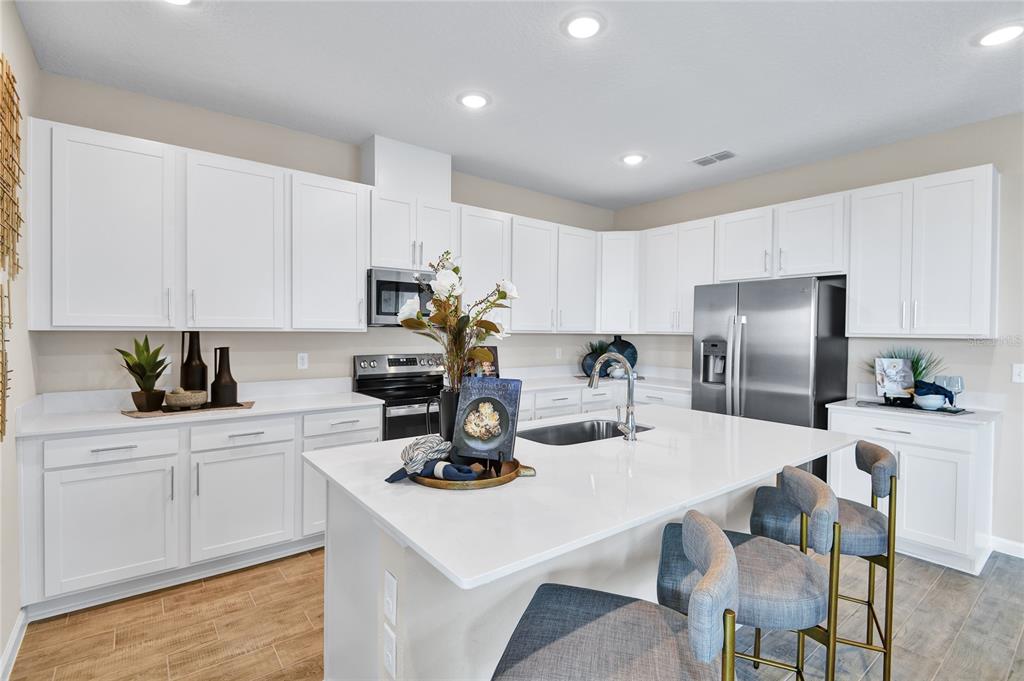 A modern kitchen features white cabinets, a large quartz island, and stainless steel appliances — 3218 WAGHORN DRIVE, TAVARES, FL