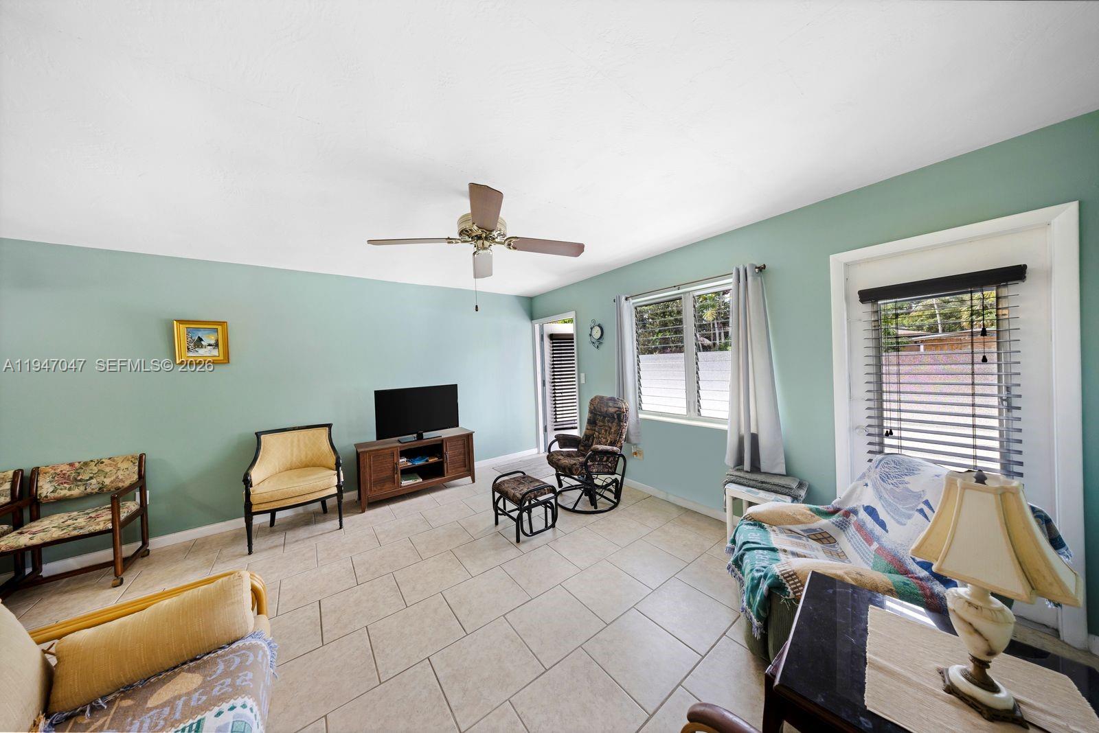 A living room features light green walls, tile flooring, a ceiling fan, and multiple chairs — 15610 NE 6th Ave # 7D, Miami FL 33162, MIAMI, FL