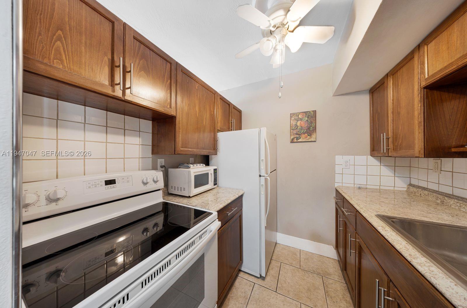 A galley kitchen features wood cabinets, granite countertops, white appliances, and tiled backsplashes — 15610 NE 6th Ave # 7D, Miami FL 33162, MIAMI, FL