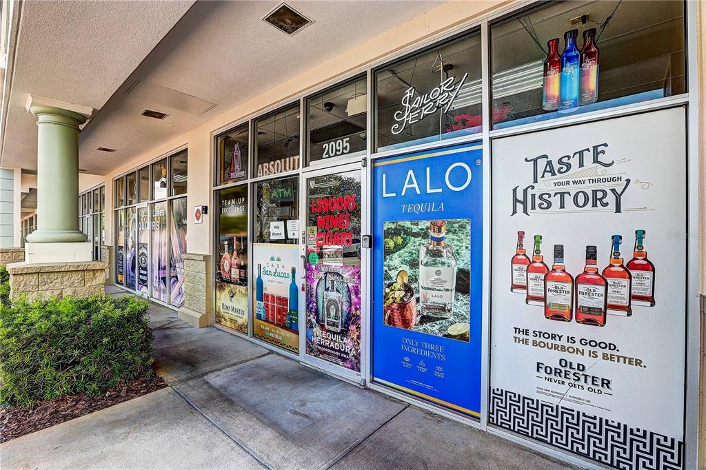 The exterior of a retail storefront features large glass windows with various liquor advertisements — COLLIER PARKWAY, LAND O LAKES, FL