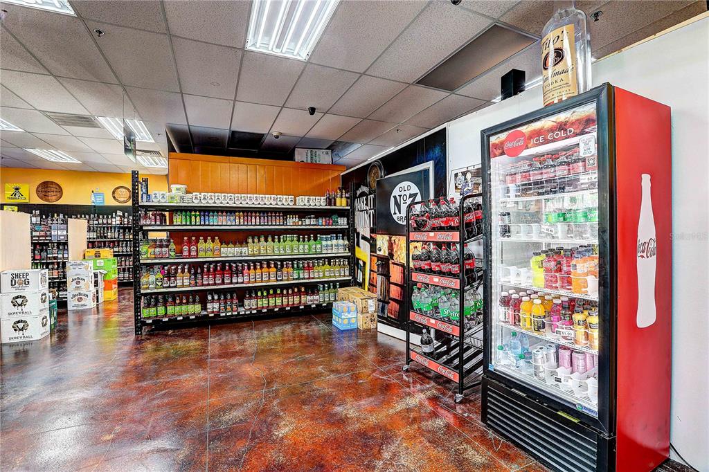 A liquor store interior features metal shelving units, a Coca-Cola refrigerator, and stained concrete floors — COLLIER PARKWAY, LAND O LAKES, FL