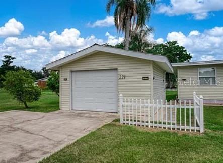 A detached garage with light-colored siding and a white fence sits on a grassy lot — 221 SPECKLED PERCH POINT, LORIDA, FL