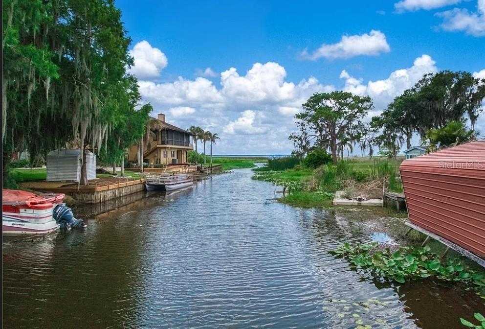 A narrow canal flows between a residential property with a boat and a metal shed — 221 SPECKLED PERCH POINT, LORIDA, FL