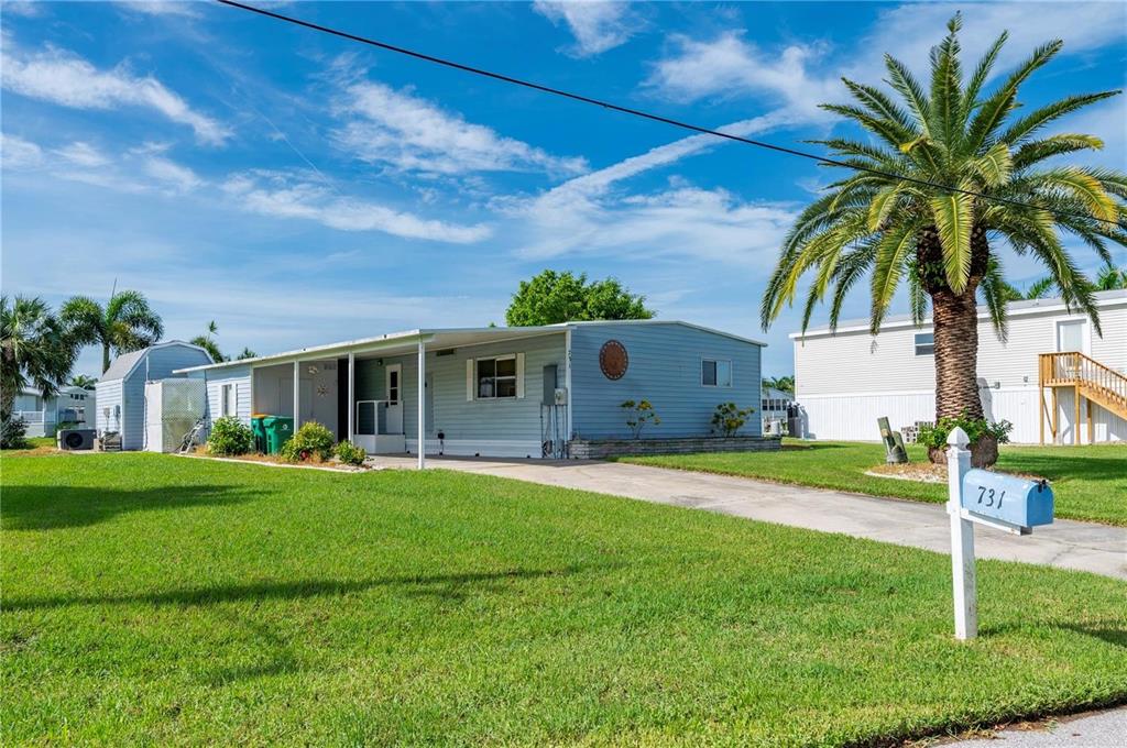 A light blue manufactured home with a covered carport sits on a grassy lot — 731 TANGERINE COURT, PUNTA GORDA, FL
