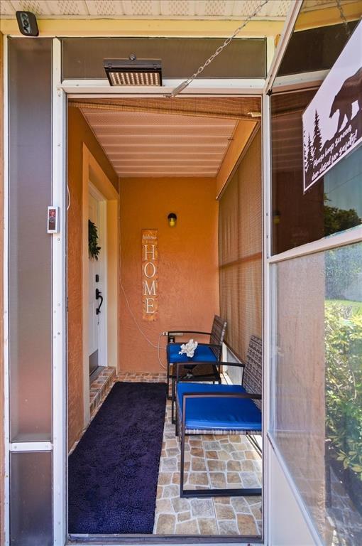 A covered porch features a stone-tiled floor, two chairs, and a vertical home sign — 7902 WATERVIEW WAY, WINTER HAVEN, FL