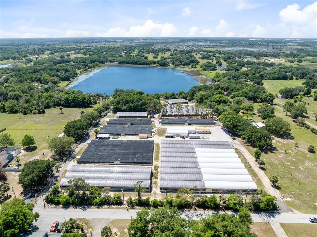 An aerial view shows a large agricultural facility with multiple greenhouses next to a lake — 18021 E APSHAWA ROAD, MINNEOLA, FL