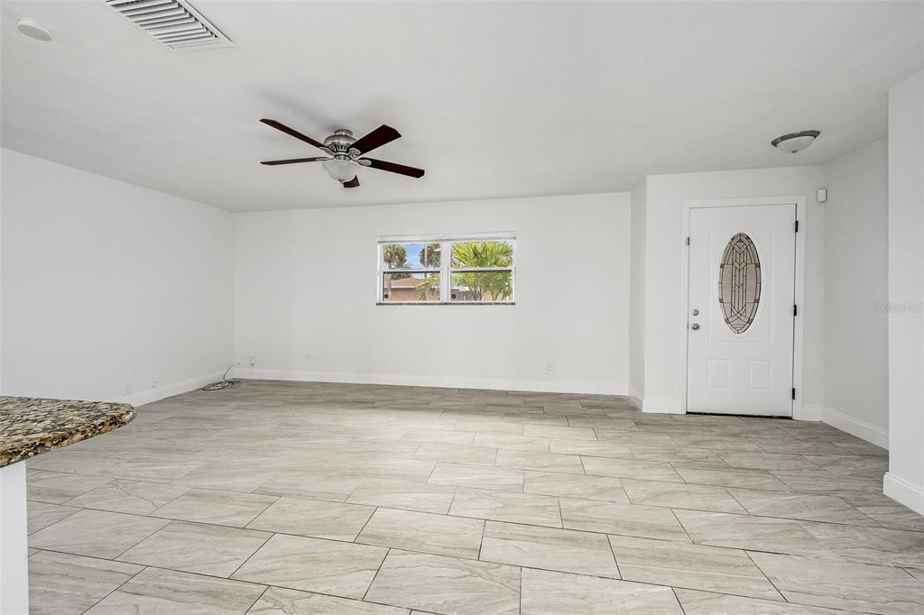 A bright, open living room features light gray tile flooring, a ceiling fan, and a front door — 1730 E RIVIERA DRIVE, MERRITT ISLAND, FL