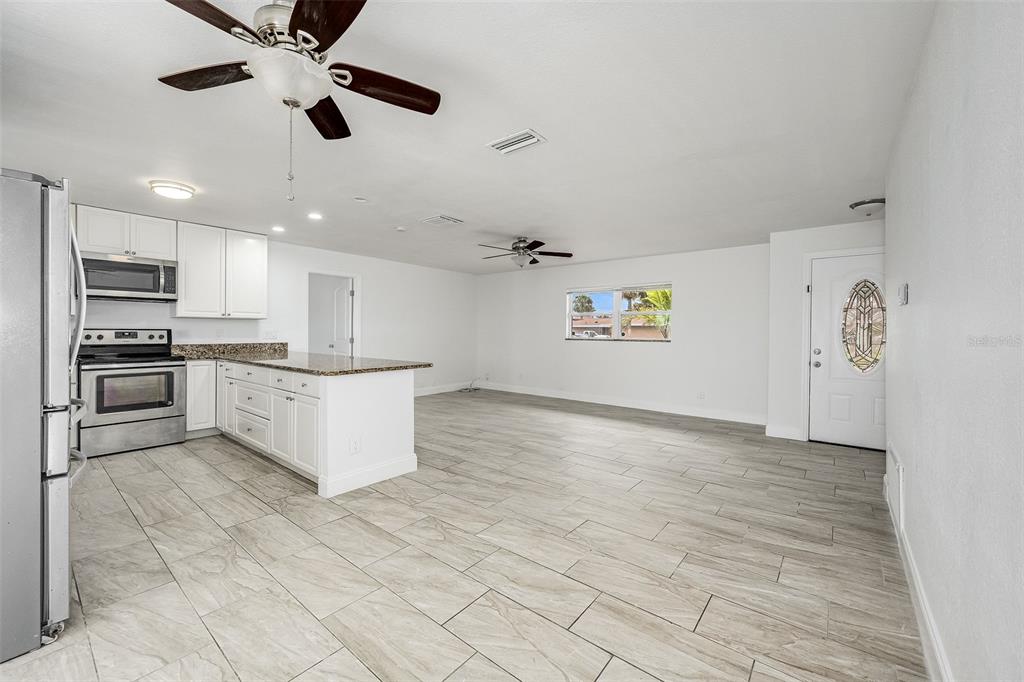 An open-concept kitchen and living area featuring white cabinets, stainless steel appliances, and tile flooring — 1730 E RIVIERA DRIVE, MERRITT ISLAND, FL