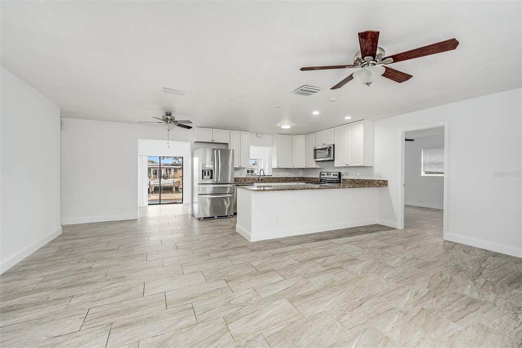 A kitchen with white cabinets, stainless steel appliances, and granite countertops opens to a living area — 1730 E RIVIERA DRIVE, MERRITT ISLAND, FL