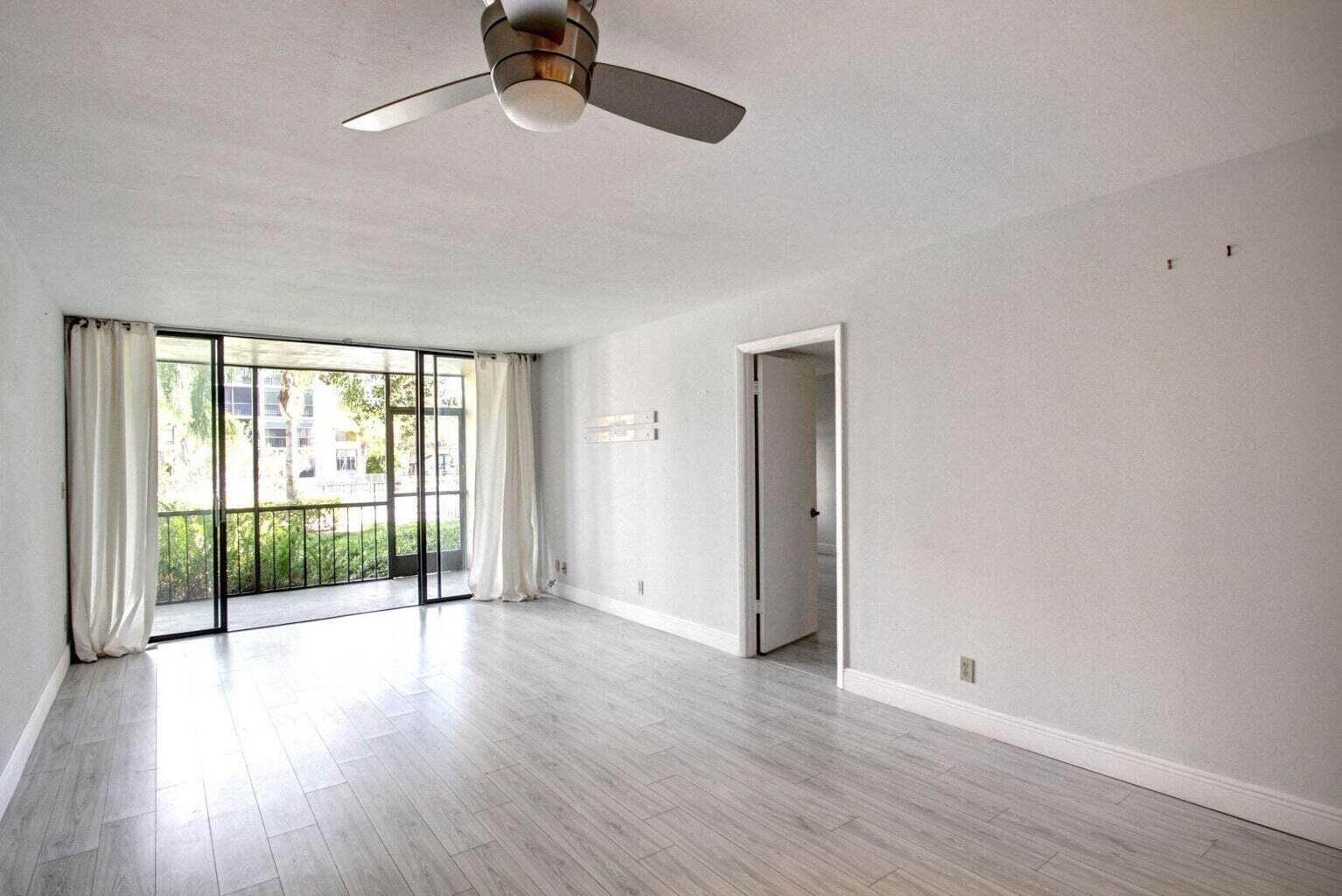 An empty living room with light wood-look flooring, a ceiling fan, and a screened balcony — 11 Royal Palm Way # 1040, Boca Raton FL 33432, BOCA RATON, FL